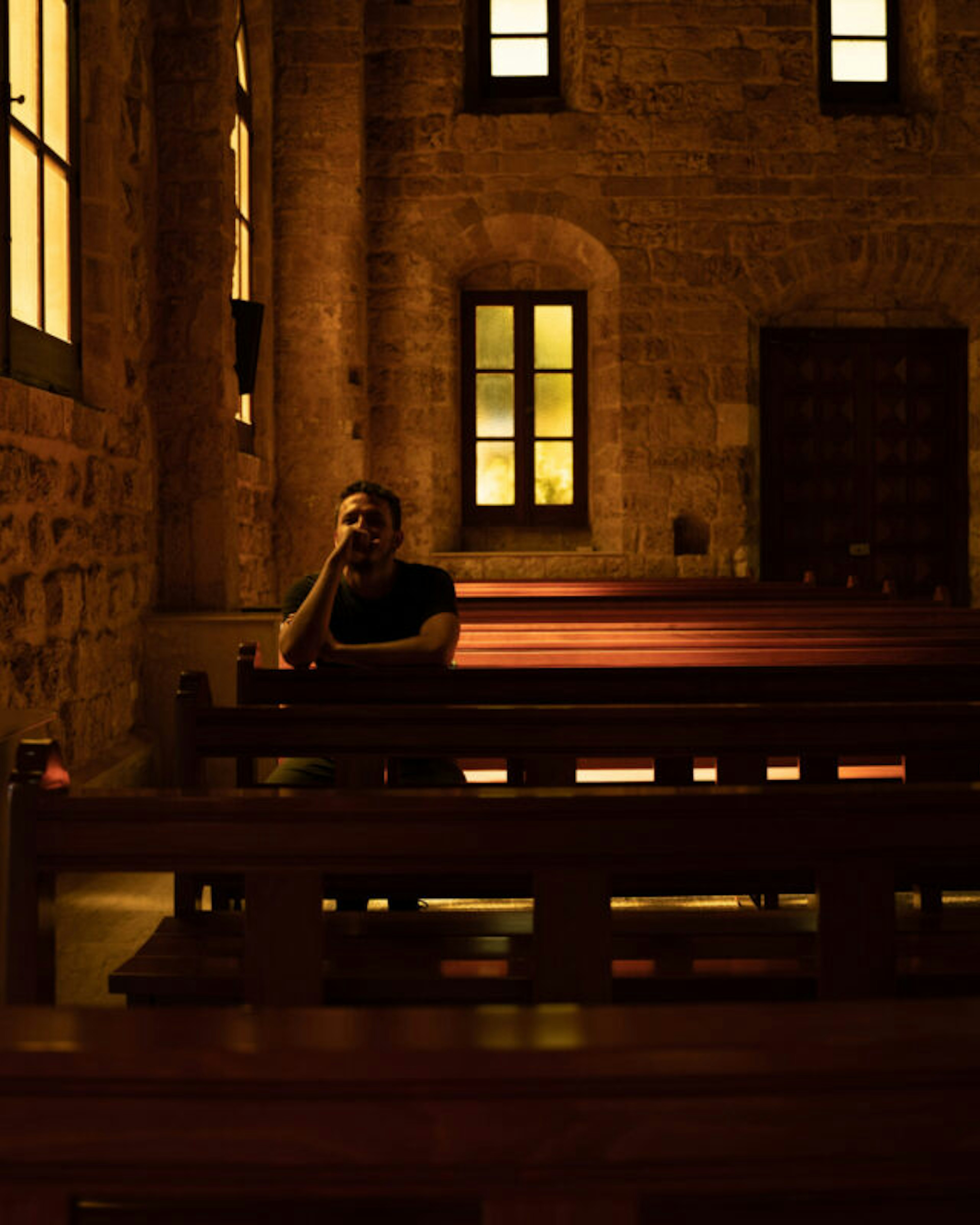 Young man is praying sitting on a bench inside of a church