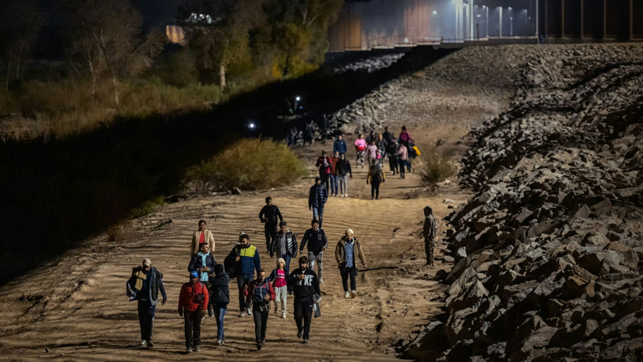 YUMA, ARIZONA - DECEMBER 30: Immigrants walk along the U.S.-Mexico border barrier on their way to await processing by the U.S. Border Patrol after crossing from Mexico on December 30, 2022 in Yuma, Arizona. (Photo by Qian Weizhong/VCG via Getty Images)