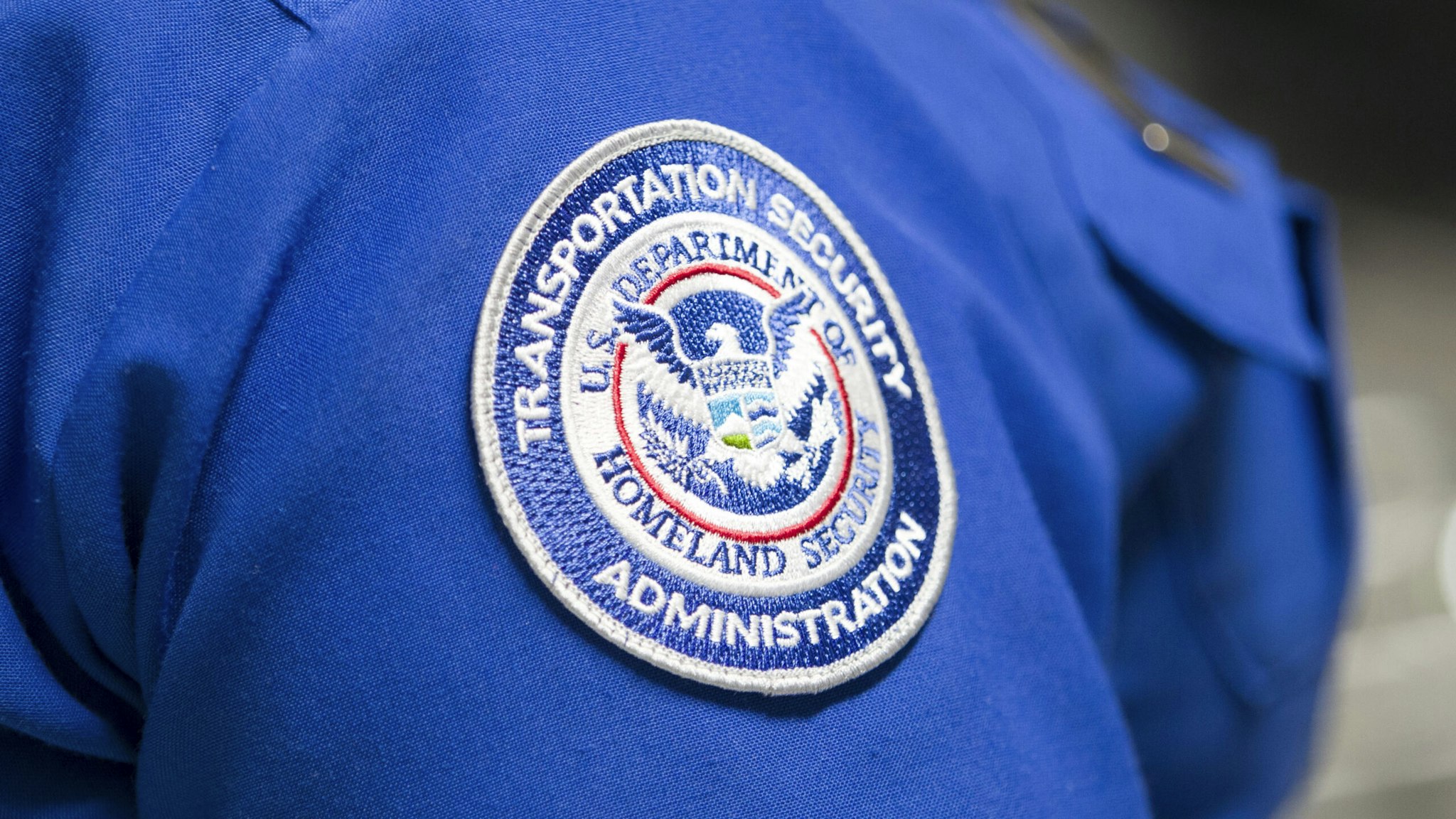 MIAMI, FLORIDA - MAY 21: A Transportation Security Administration (TSA) agent's patch is seen as she helps travelers place their bags through the 3-D scanner at the Miami International Airport on May 21, 2019 in Miami, Florida. TSA has begun using the new 3-D computed tomography (CT) scanner in a checkpoint lane to detect explosives and other prohibited items that may be inside carry-on bags.