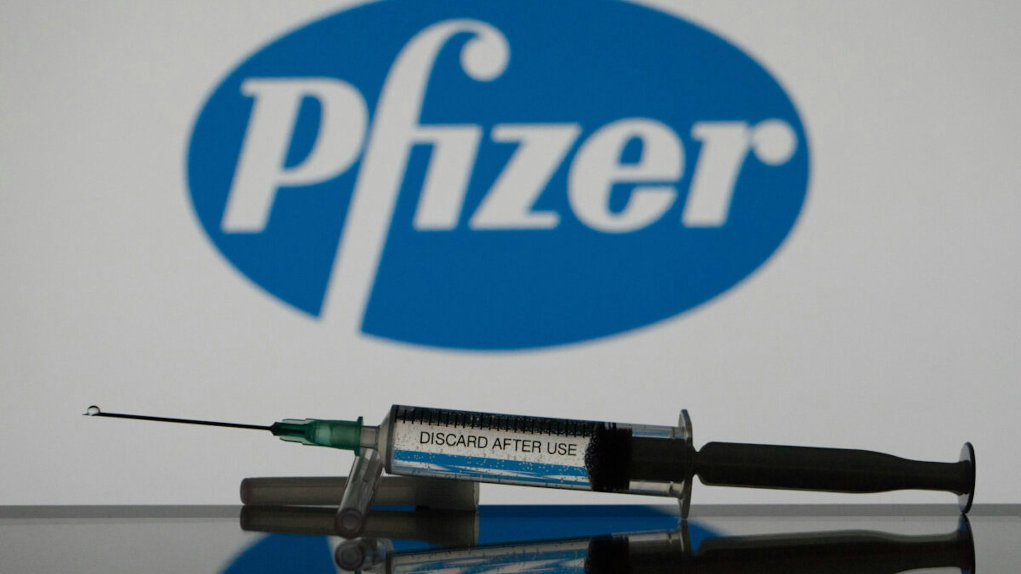 In this photo illustration a covid-19 vaccine is seen with the Pfizer logo in the background.