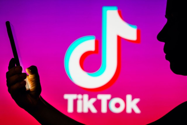 BRAZIL - 2023/04/06: In this photo illustration, a woman's silhouette holds a smartphone with the TikTok logo in the background.