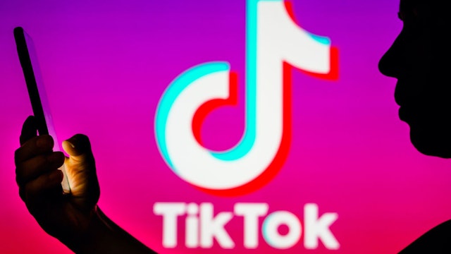 BRAZIL - 2023/04/06: In this photo illustration, a woman's silhouette holds a smartphone with the TikTok logo in the background.
