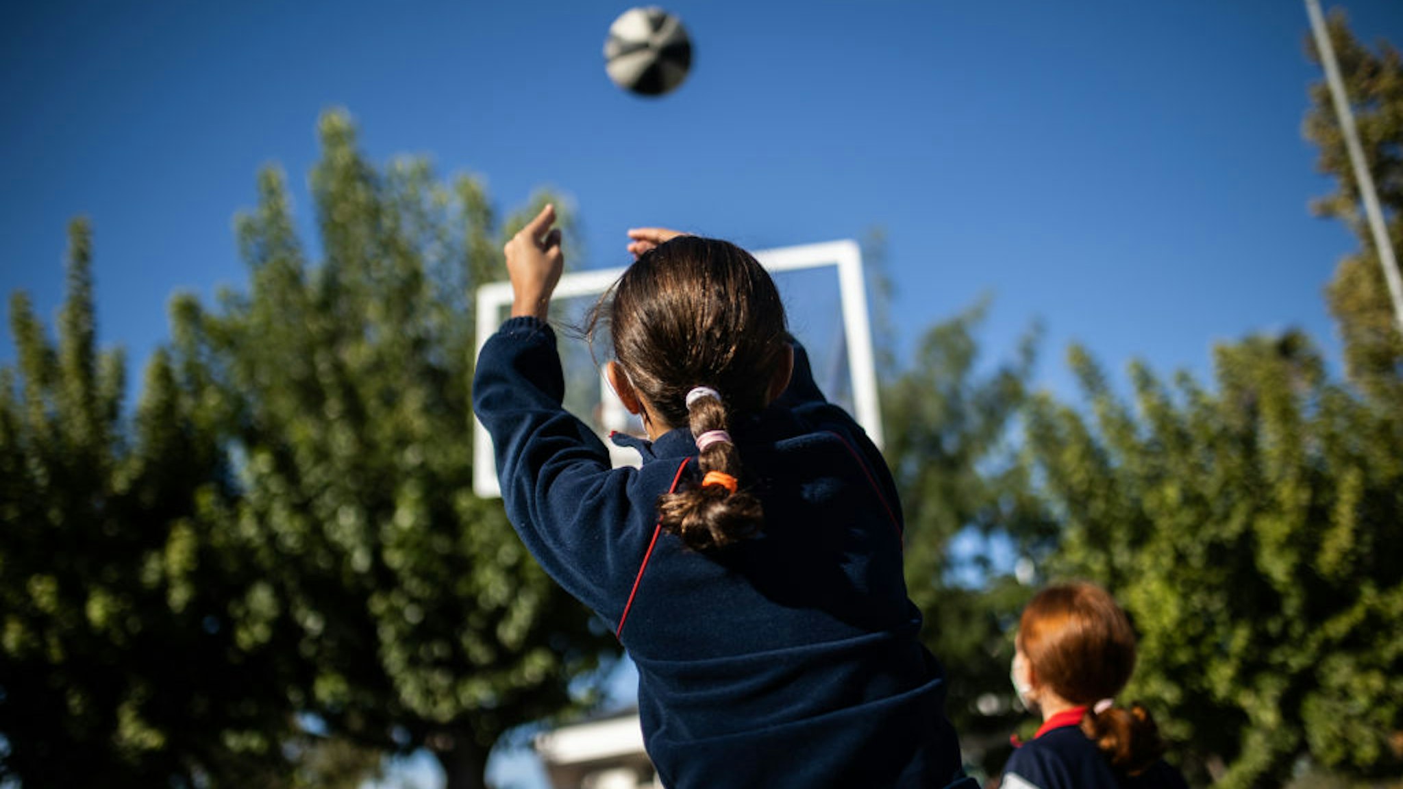 MADRID, SPAIN - OCTOBER 25: A girl plays basketball in the courtyard of the Alameda de Osuna School on the day that comes into force the measure that allows not wearing masks in school playgrounds in Madrid, on 25 October, 2021 in Madrid, Spain. With this permission, which comes into force this Monday, Madrid becomes the first autonomous community that allows not wearing masks in school playgrounds in the region, at recess and outdoors, as long as the interpersonal safety distance established by the pandemic is respected. This measure, implemented by the Community of Madrid, has been criticized by Health, who recalled that you can not unilaterally decide to remove the mask in school playgrounds as the law in force since March 29 establishes the mandatory use in outdoor spaces where it is not possible to maintain a minimum distance of 1.5 meters. (Photo By Alejandro Martinez Velez/Europa Press via Getty Images)