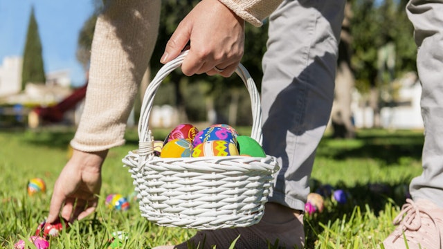 Close up of female holding an easter egg basket and hiding eggs in the grass on an out of focus background. Selective focus. Easter concept.
