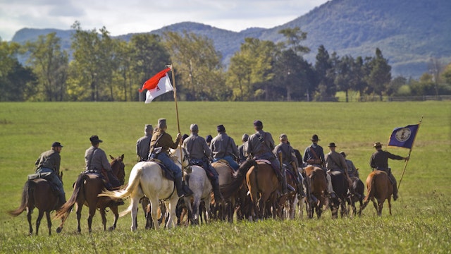 A troop of Confederate Cavalry ride across the battlefield at Cedar Creek in the Shenandoah Valley of Virginia during a reenactment. The flag carried by the rider at the far right of the picture is the state flag of Virginia.