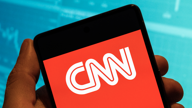 CHINA - 2023/02/19: In this photo illustration, the American news-based pay television channel CNN logo is seen displayed on a smartphone with an economic stock exchange index graph in the background.