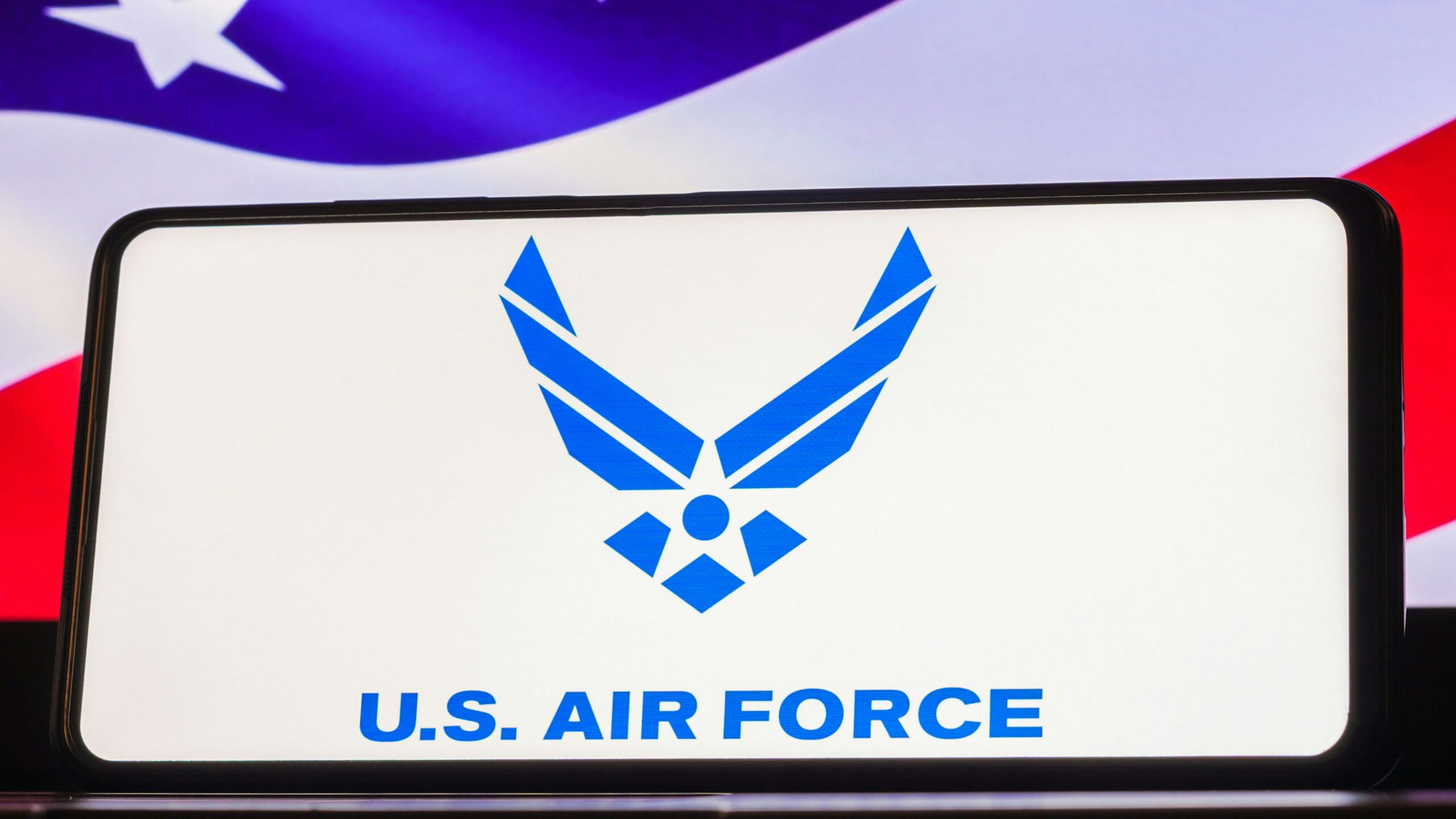 BRAZIL - 2023/03/22: In this photo illustration, the United States Air Force (USAF) logo seen displayed on a smartphone screen, United States of America flag in the background.