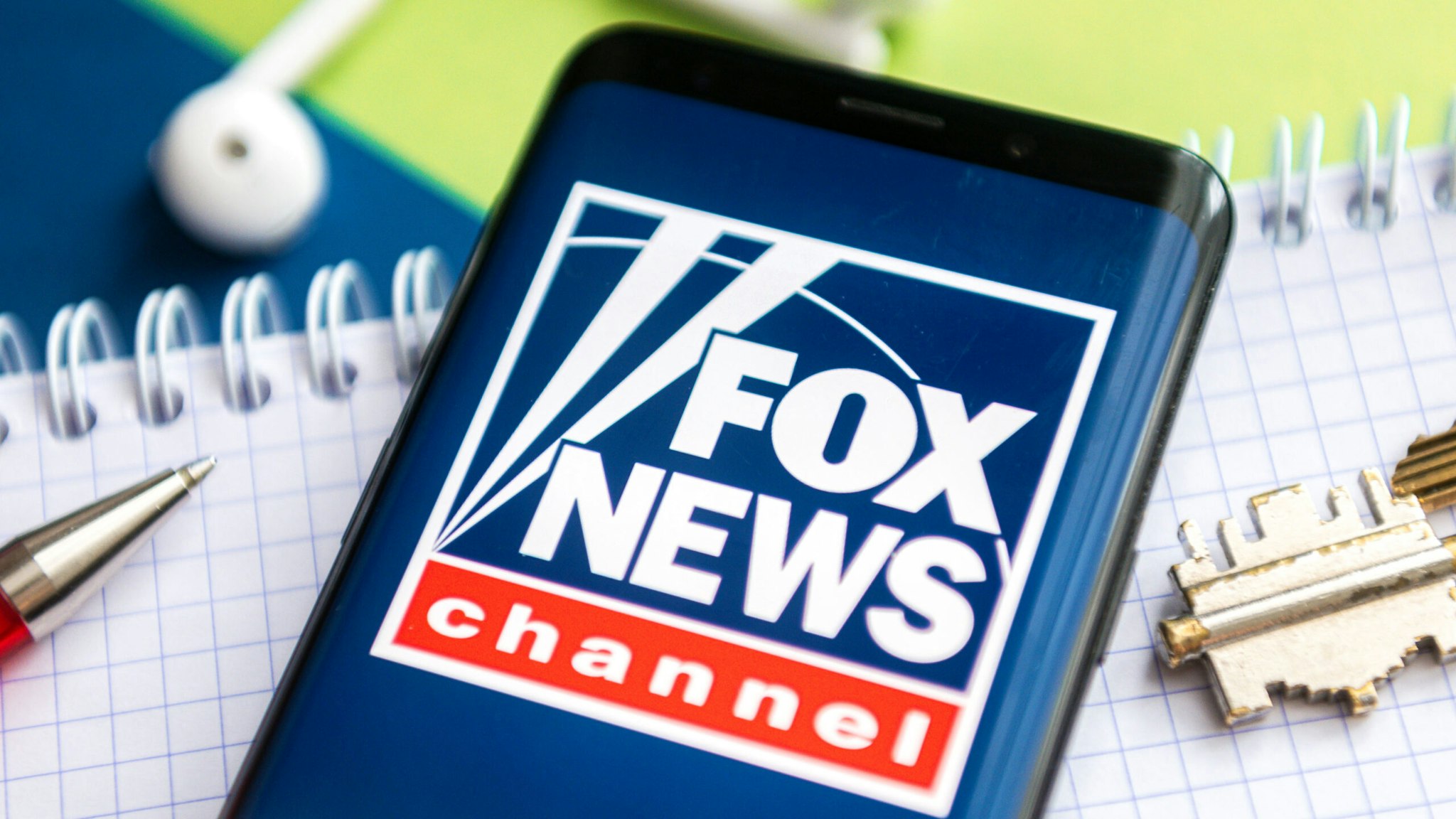 POLAND - 2021/02/09: In this photo illustration, a Fox News logo seen displayed on a smartphone with a pen, key, book and headsets in the background.