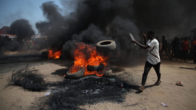 TOPSHOT - A man throws a tyre a bonfire on the Kaduna-Abuja highway in Gauruka, near Abuja, Nigeria, on May 24, 2021 during a protest against incessant kidnapping and killing after gunmen kidnapped 16 residents and killed three others in Niger State.