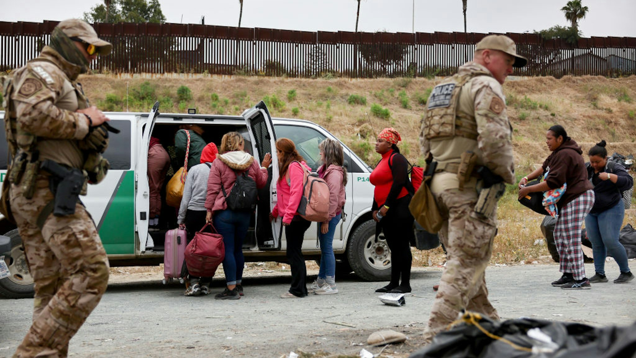 SAN DIEGO, CALIFORNIA - MAY 13: Customs and Border Protection officers walk as immigrants enter a vehicle to be transported from a makeshift camp between border walls, between the U.S. and Mexico, on May 13, 2023 in San Diego, California. Some of the immigrants at the open air camp have been waiting for days in limbo for a chance to plead for asylum while local volunteer groups are providing food and other necessities. The U.S. government's Covid-era Title 42 policy, which for the past three years had allowed for the quick expulsion of irregular migrants entering the country, expired on the evening of May 11. (Photo by Mario Tama/Getty Images)