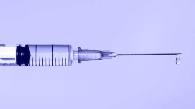 Disposable sterile syringe with drop of fluid medication on thin needle on violet background.