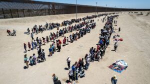 EL PASO, TEXAS - MAY 11: In an aerial view, immigrants line up to be processed to make asylum claims at a makeshift migrant camp on May 11, 2023 in El Paso, Texas. The number of immigrants reaching the border has surged with the end of the U.S. government's Covid-era Title 42 policy, which for the past three years has allowed for the quick expulsion of irregular migrants entering the country.