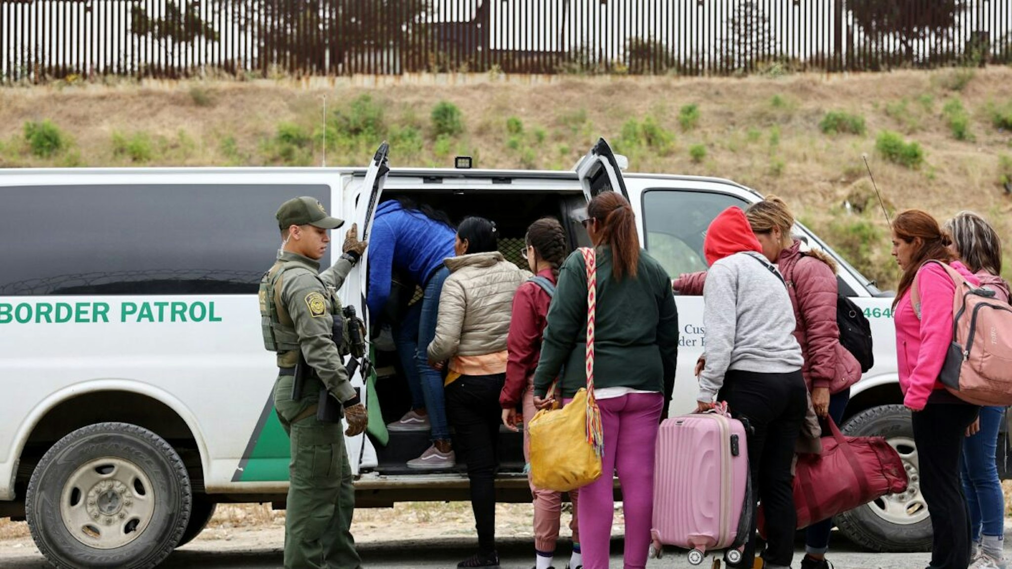 A U.S. Border Patrol agent keeps watch as immigrants enter a vehicle to be transported from a makeshift camp between border walls, between the U.S. and Mexico, on May 13, 2023 in San Diego, California.
