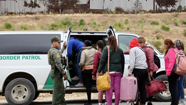 A U.S. Border Patrol agent keeps watch as immigrants enter a vehicle to be transported from a makeshift camp between border walls, between the U.S. and Mexico, on May 13, 2023 in San Diego, California.