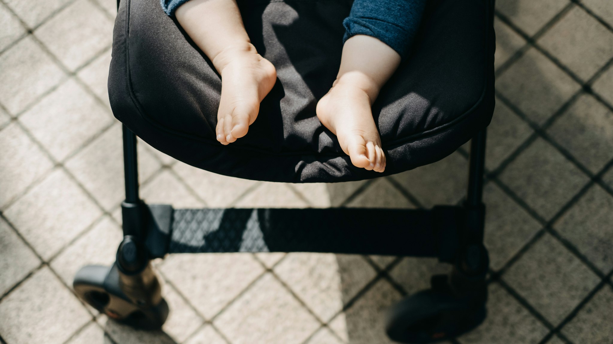 Low section of baby feet resting in baby stroller on street with warmth of sunlight - stock photo