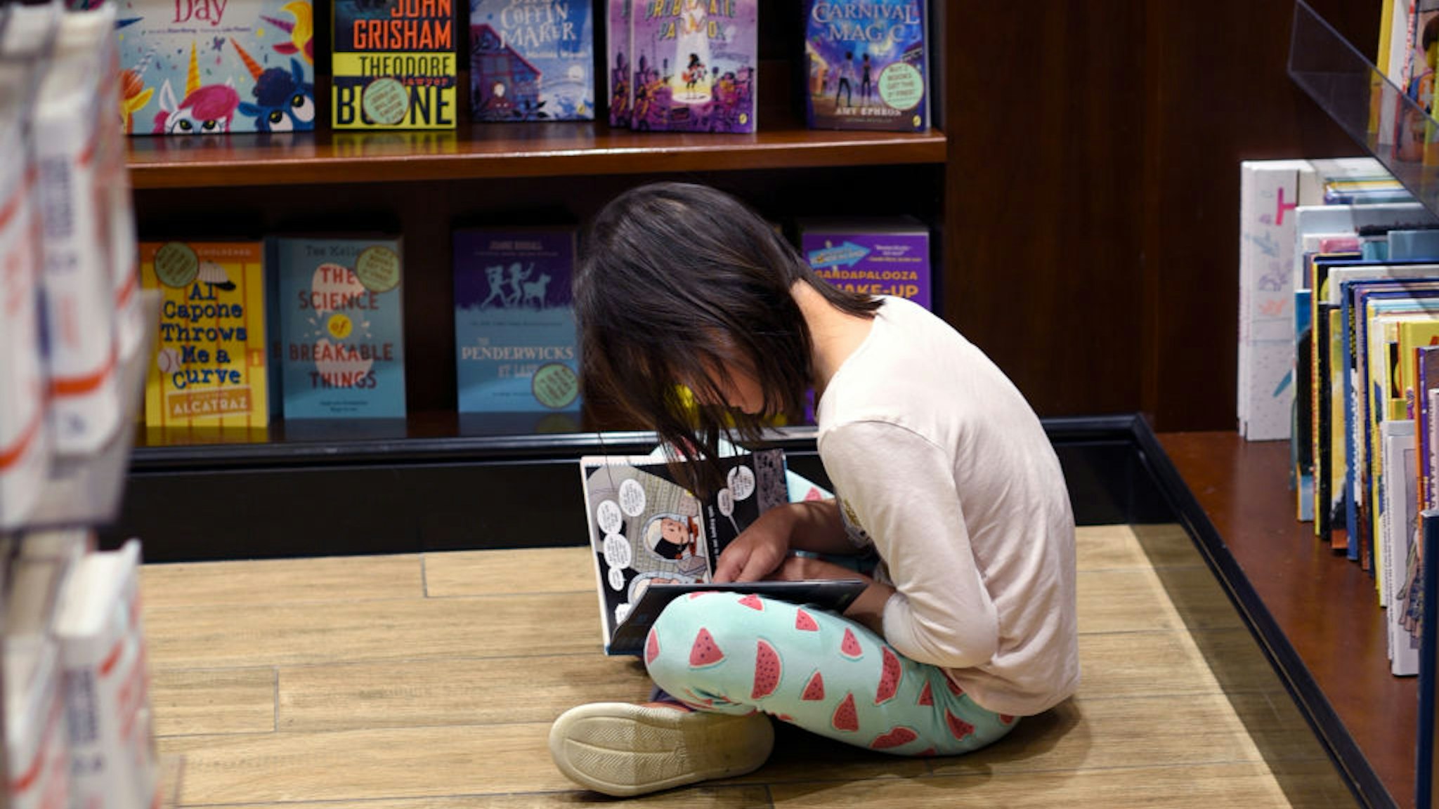 DENVER, COLORADO - JUNE 20, 2019: A young girl sits on the floor and reads as her mother shops in a bookstore located in the terminal at Denver International Airport in Denver, Colorado. (Photo by Robert Alexander/Getty Images)