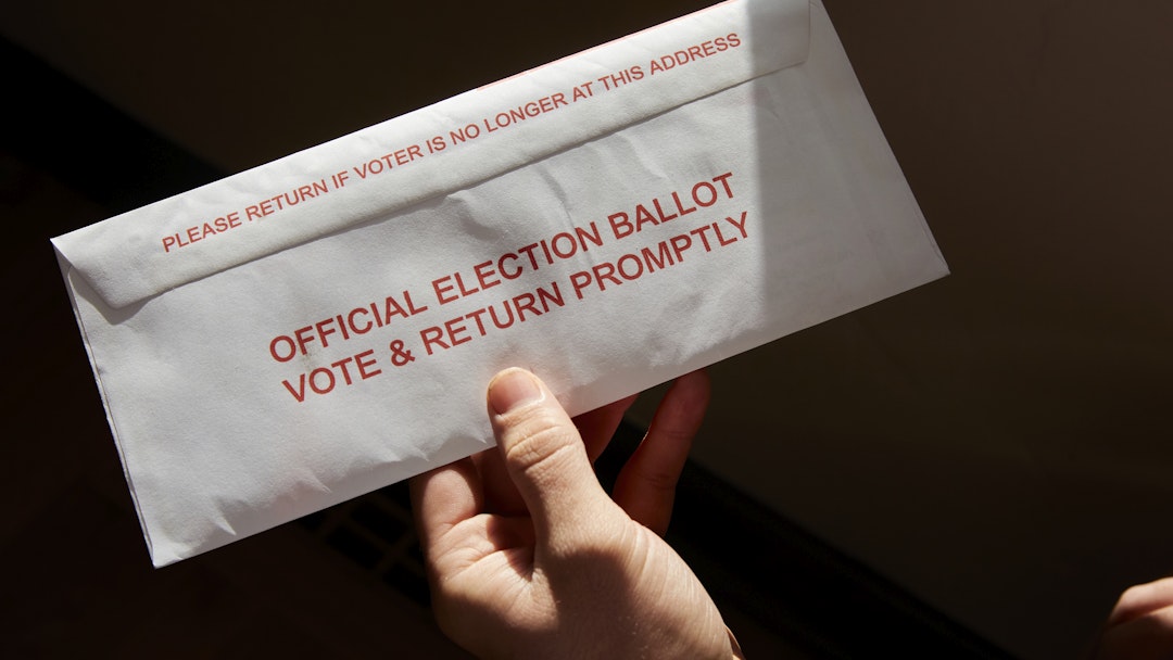 A person standing inside his home holding his mail in voting ballot
