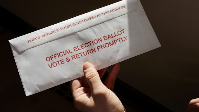 A person standing inside his home holding his mail in voting ballot