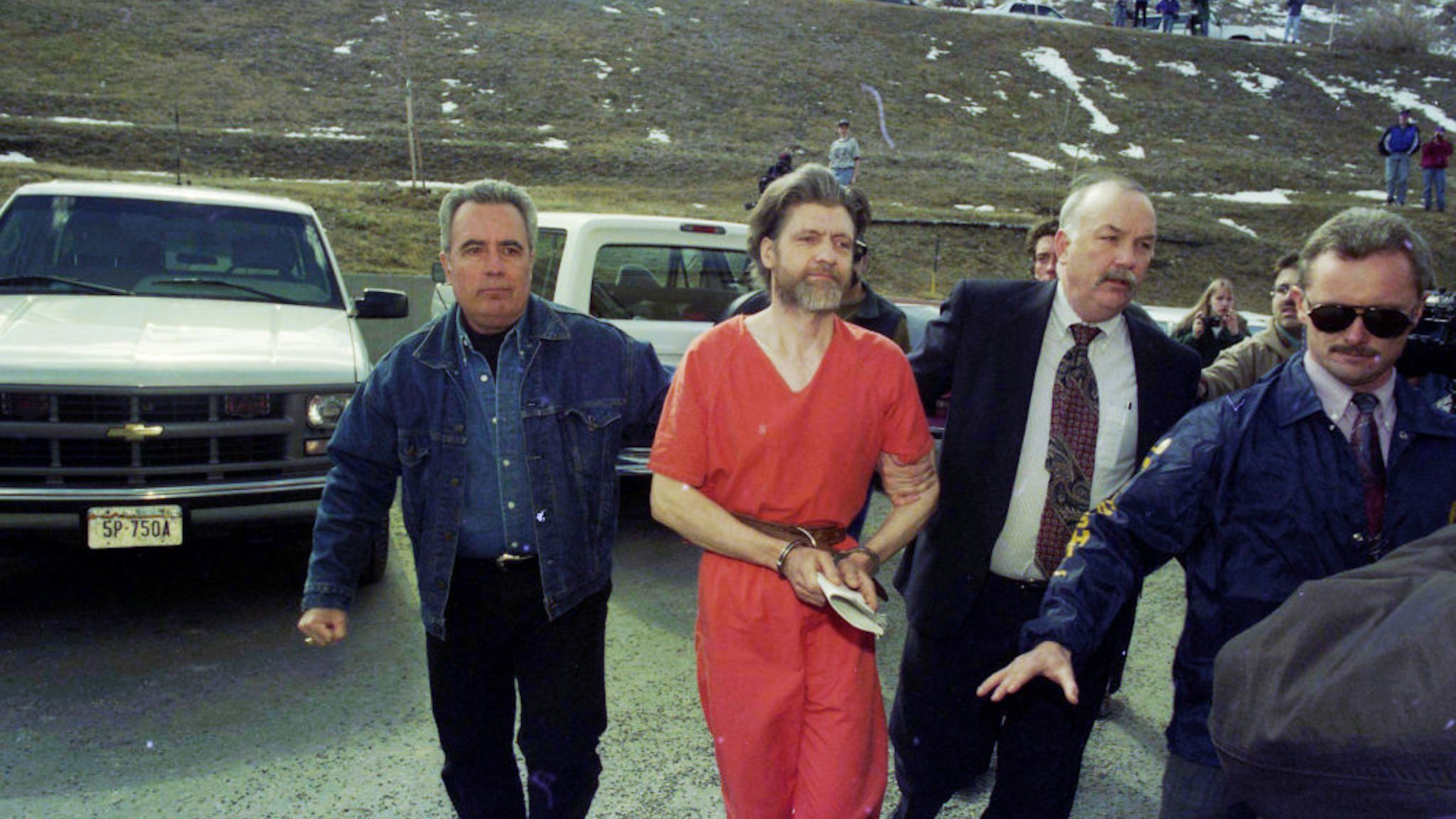 Theodore 'Ted' Kaczynski (in orange) is guided to his arraignment by federal marshals, Helena, Montana, April 4, 1996. He had been arrested in connection with the 'Unabomber' bombings and the deaths those explosions caused.