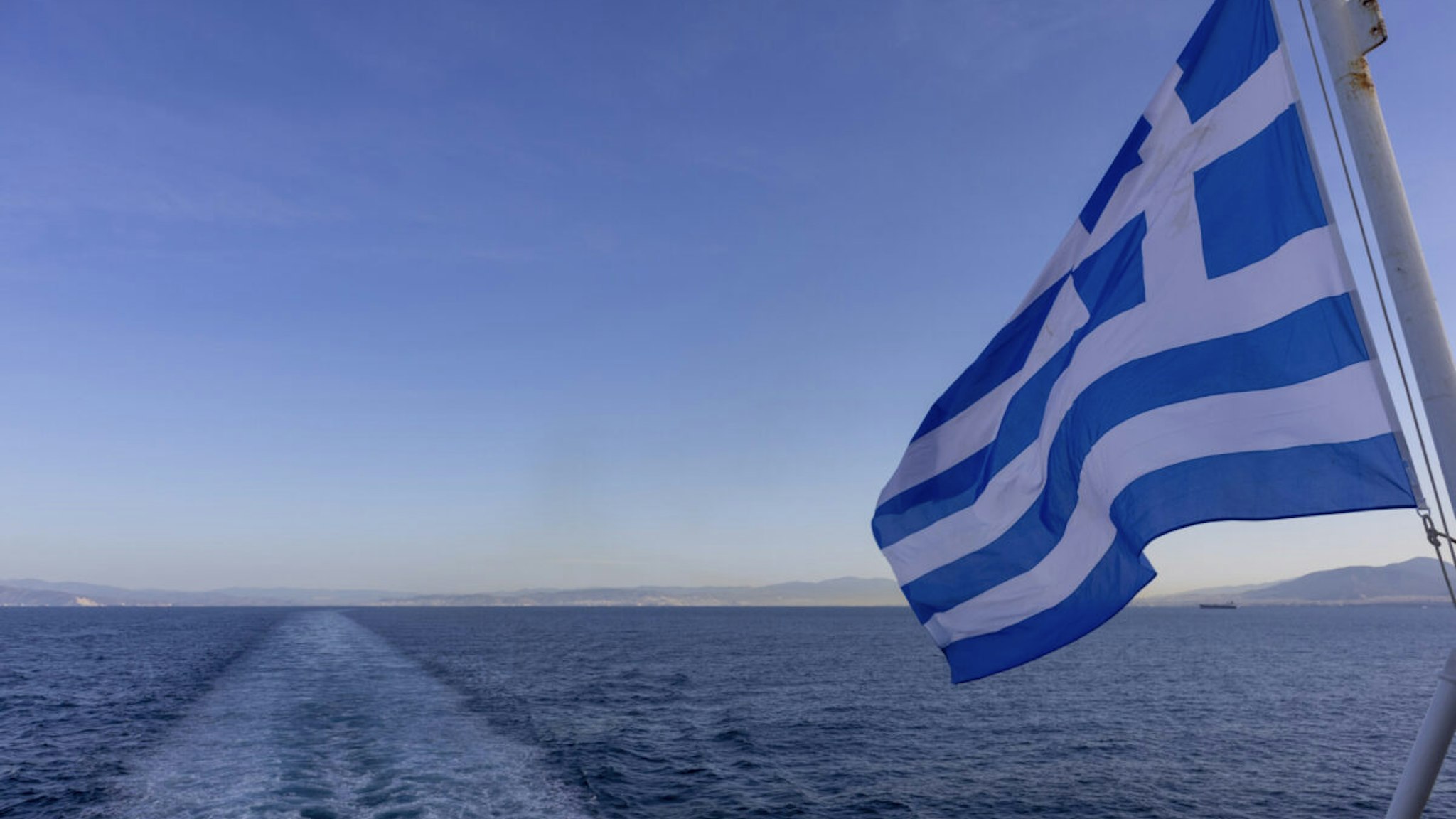 TINOS, GREECE - APRIL 14: View of greek flag from ship leaving the port Tino island on April 14, 2021 in Tinos, Greece.