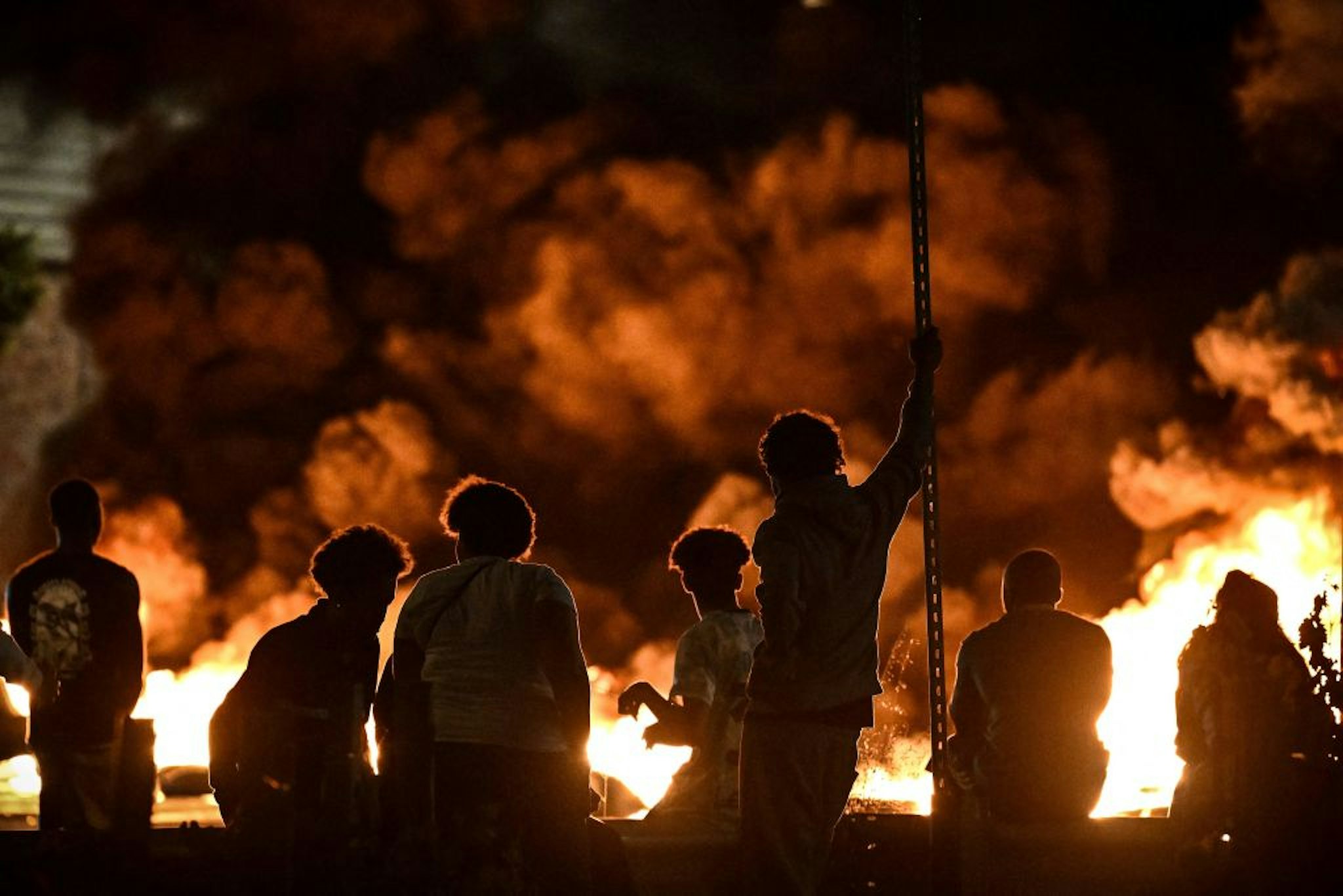 TOPSHOT - People look at burning tyres blocking a street in Bordeaux,, south-western France on late June 29, 2023, during riots and incidents nationwide after the killing of a 17-year-old boy by a police officer's gunshot following a refusal to comply in a western suburb of Paris. (Photo by Philippe LOPEZ / AFP)