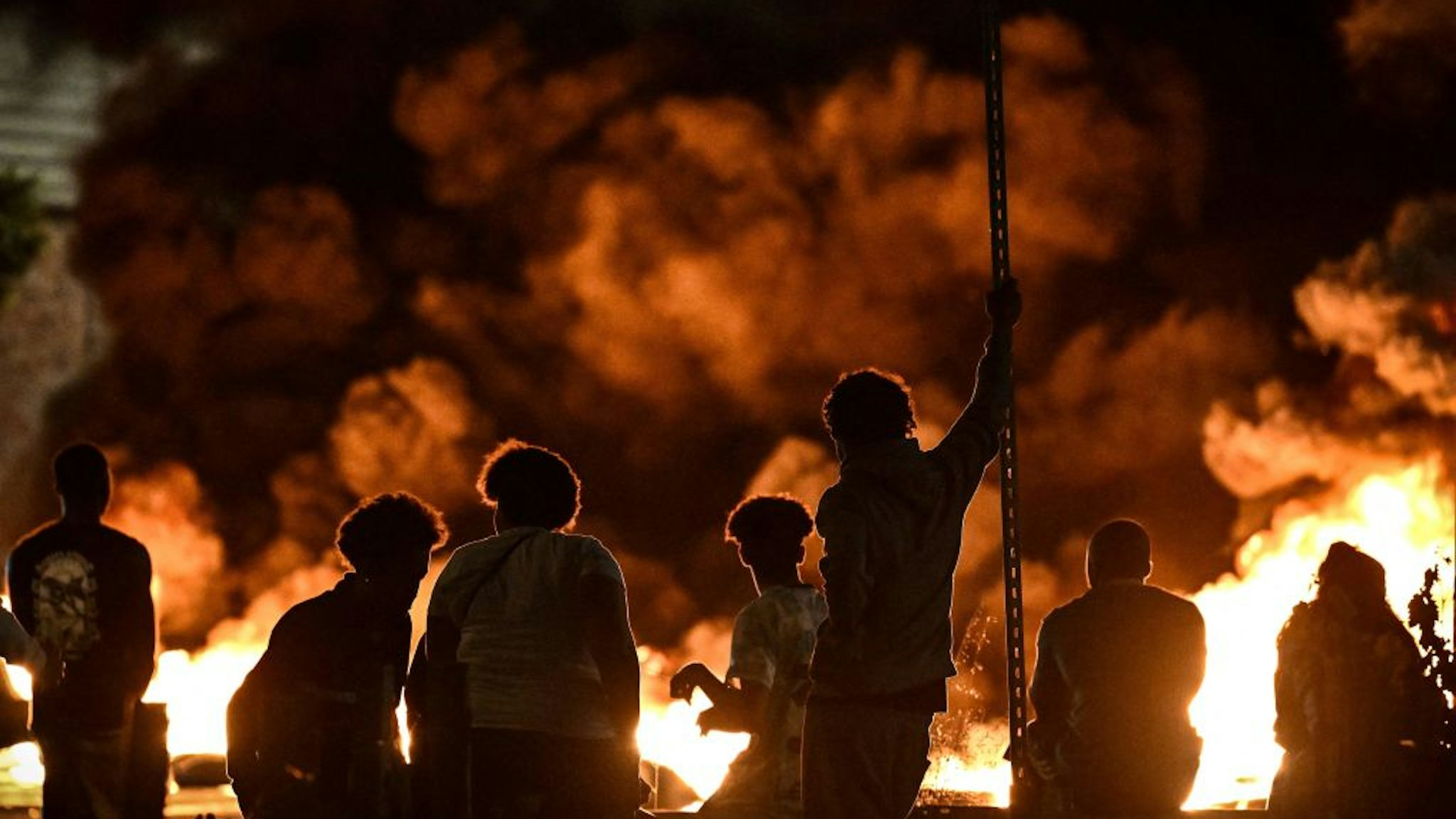 TOPSHOT - People look at burning tyres blocking a street in Bordeaux,, south-western France on late June 29, 2023, during riots and incidents nationwide after the killing of a 17-year-old boy by a police officer's gunshot following a refusal to comply in a western suburb of Paris. (Photo by Philippe LOPEZ / AFP)