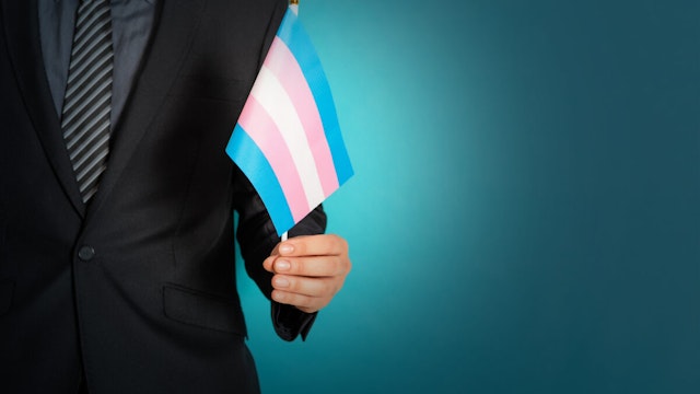 A businessman hand holding a flag in transgender pride colors