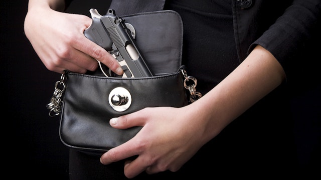 A close-up of a woman holding a handgun in a purse.