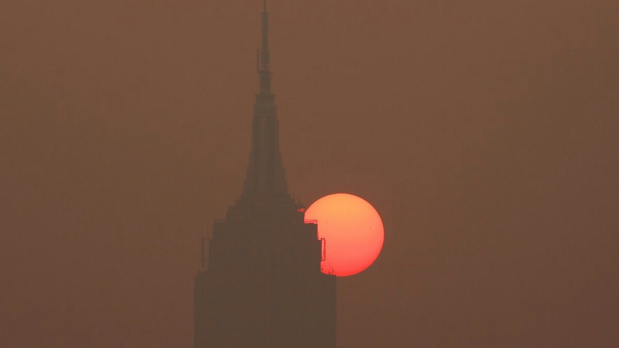The sun is shrouded as it rises in a smokey sky behind the Empire State Building in New York City on June 8, 2023, as seen from Jersey City, New Jersey.