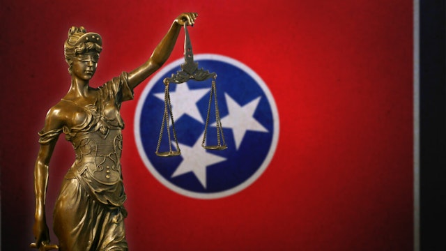 Close-up of a small bronze statuette of Lady Justice before a flag of Tennessee.