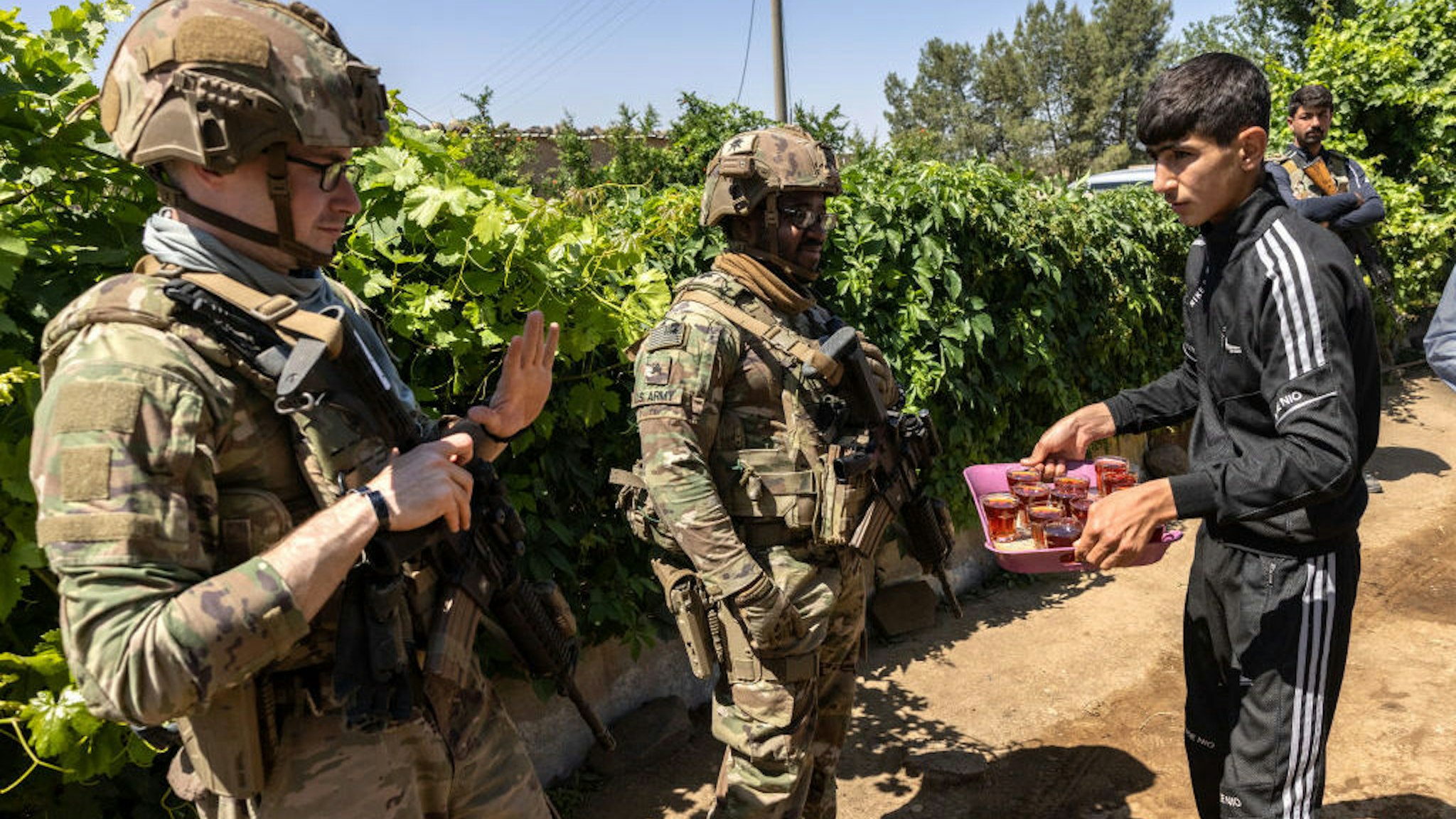 A U.S. Army soldier declines the offer of tea as his commanding officer and allied troops meet with local villagers on May 26, 2021 near the Turkish border in northeastern Syria. U.S. forces, part of Task Force WARCLUB operate from remote combat outposts in the area, coordinating with the Kurdish-led Syrian Democratic Forces (SDF) in combatting residual ISIS extremists and deterring pro-Iranian militia. (Photo by John Moore/Getty Images)