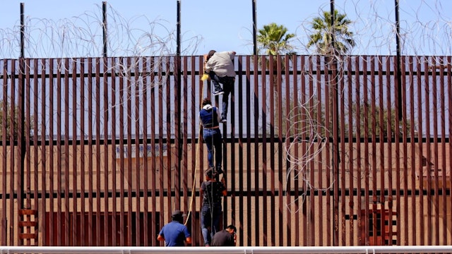 Migrants attempt to climb over the border wall from Mexicali, Mexico to Calexico, USA, along the U.S.-Mexico border near the port of entry on Saturday, May 13, 2023 in Mexicali, Baja California.