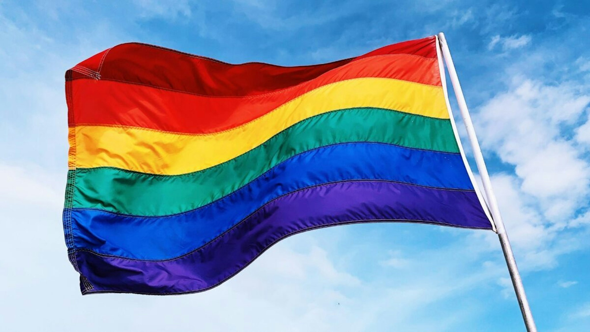 Rainbow flag waving in the wind against blue sky