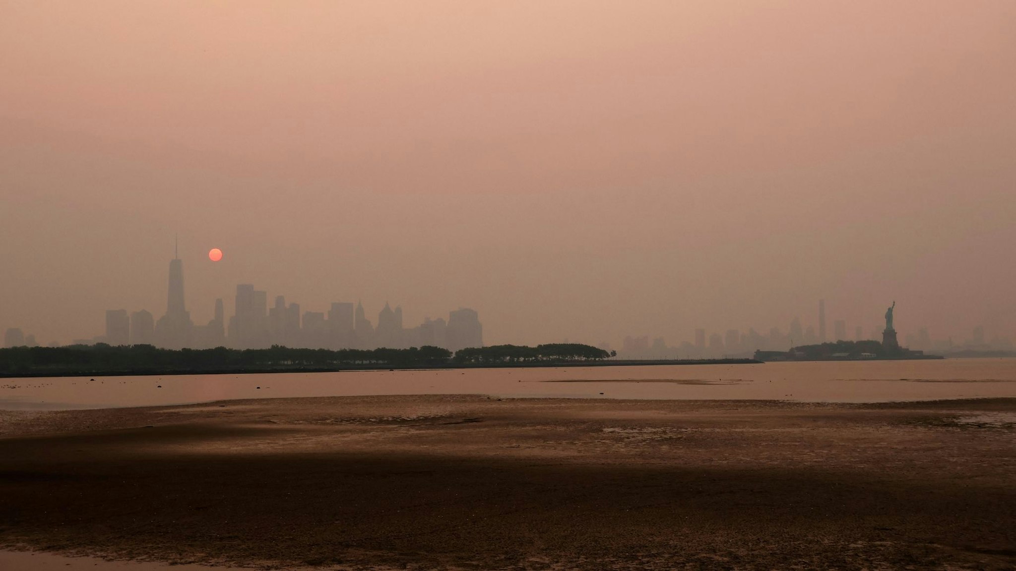 JERSEY CITY, NJ - JUNE 7: Smoke continues to shroud the sun as it rises behind the skyline of lower Manhattan, Brooklyn and the Statue of Liberty in New York City on June 7, 2023, as seen from Jersey City, New Jersey.
