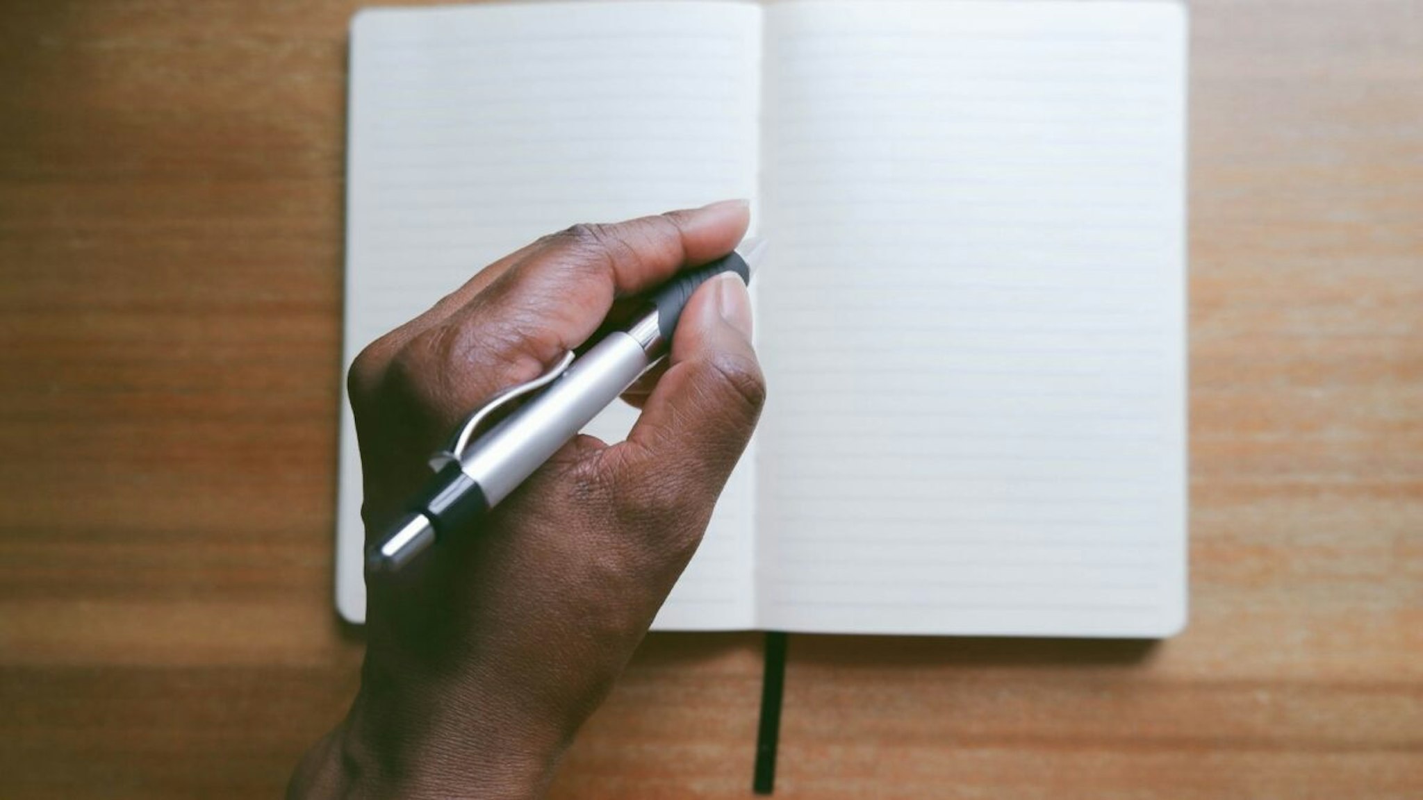 Close-up of unrecognizable black woman writing in notebook at desk