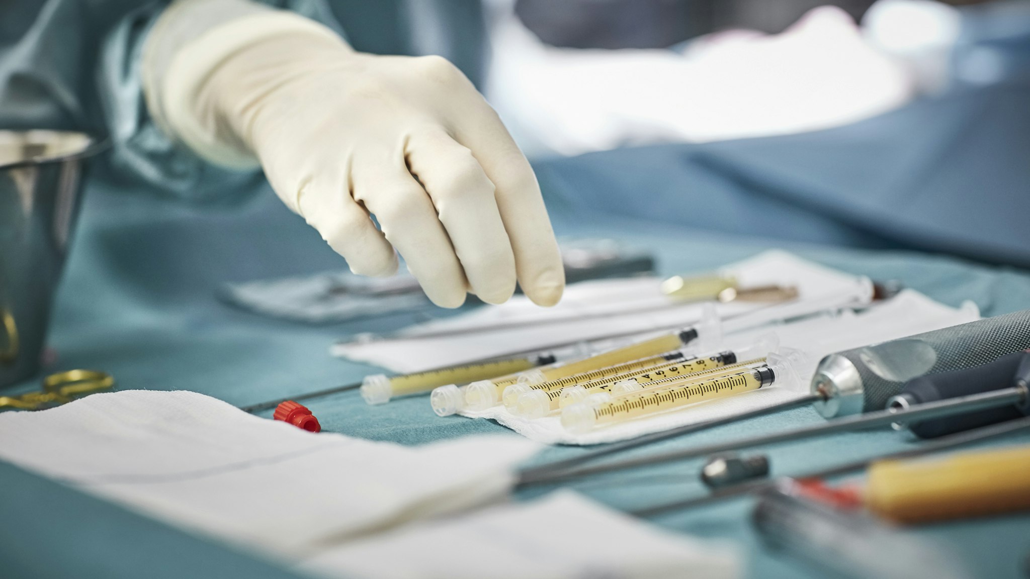 Cropped image of female surgeon reaching for syringes on table. Close-up of healthcare worker's hand wearing surgical glove. She is in emergency room