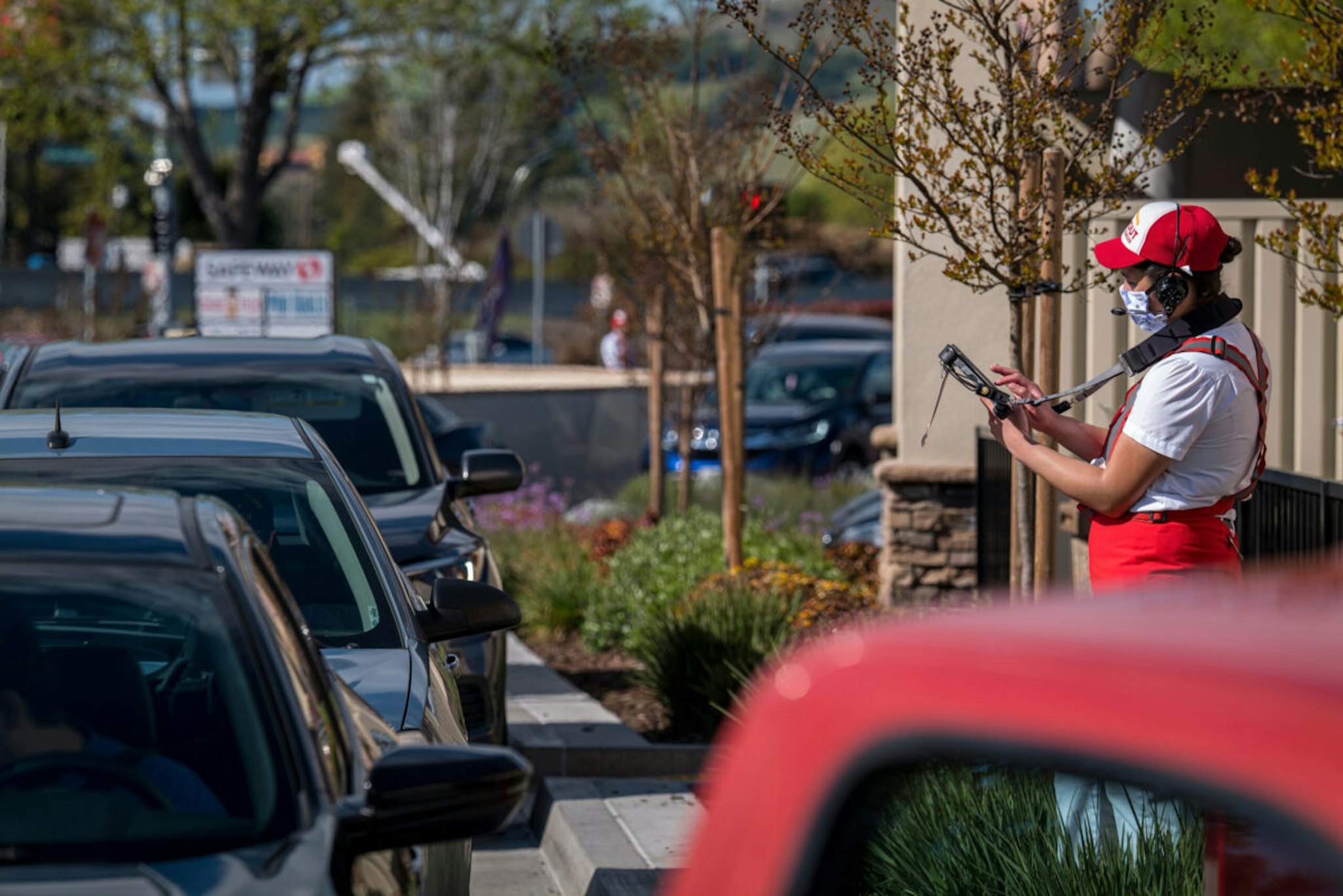 A worker wearing a cloth protective mask takes an order from a customer waiting in a drive-thru line at an In-N-Out Burgers restaurant in Vallejo, California, U.S., on Tuesday, April 7, 2020.