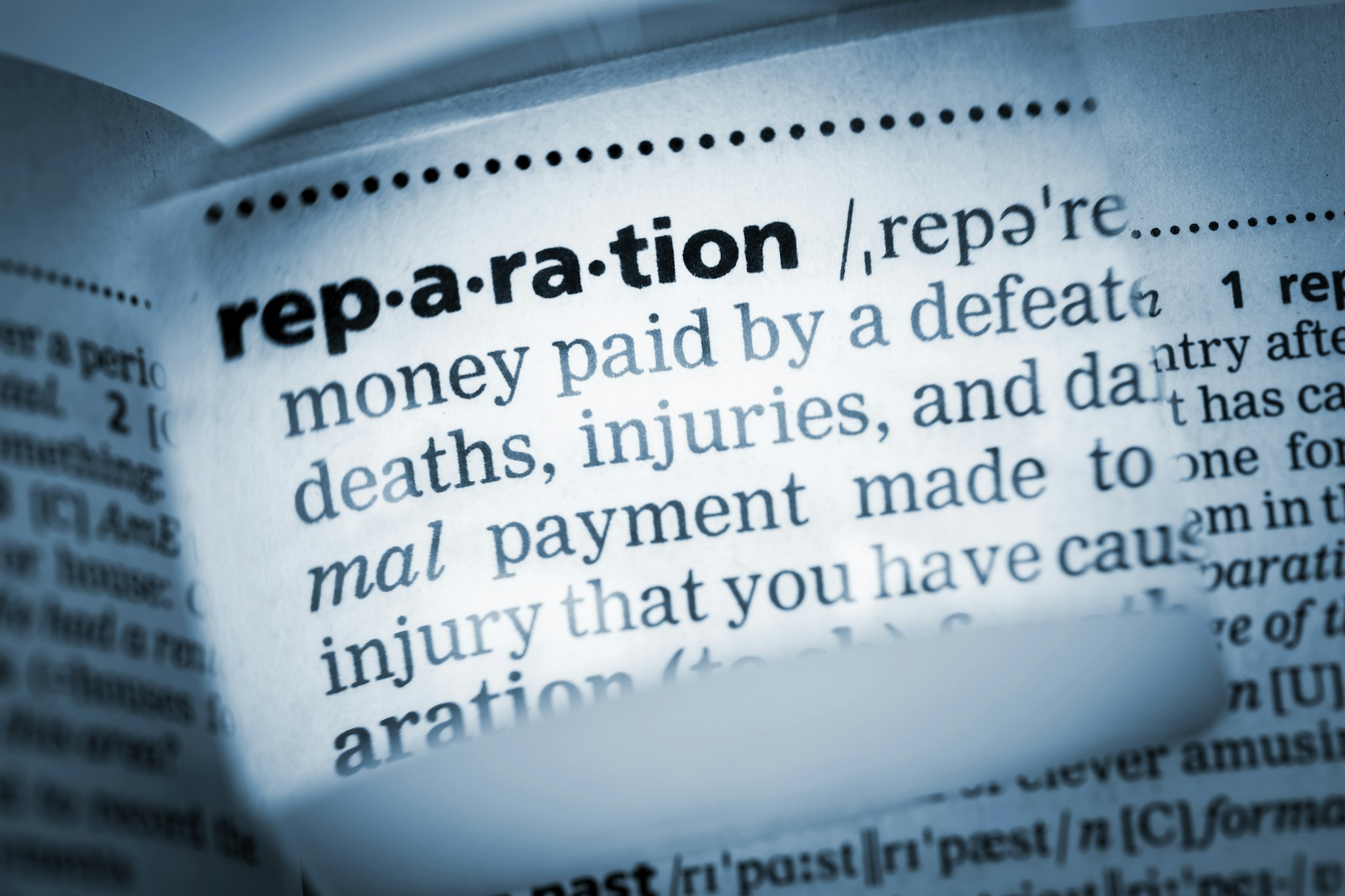 The Dictionary definition of the word “reparation” photo taken through magnifying glass from a page of a dictionary with selective focus.