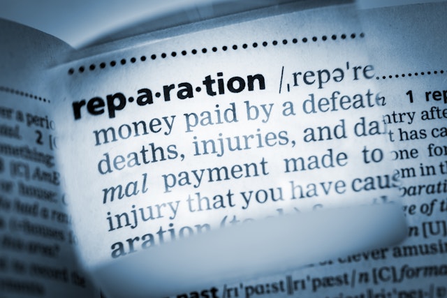 The Dictionary definition of the word “reparation” photo taken through magnifying glass from a page of a dictionary with selective focus.