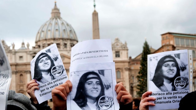 ROME, ITALY - DECEMBER 18: Demonstrators with Emanuela Orlandi's photo in the background St. Peter's Basilica during the Silent demonstration from Castel Sant'Angelo to St. Peter's Square to shed light on the kidnapping of Emanuela Orlandi who disappeared 29 years ago, and to recall the petition launched to Pope Benedict XVI to demand the truth, which has reached 40 thousand adhesions. The event was organised by Pietro Orlandi, Emanuela's brother.on December 18, 2011 in Rome, Italy. Emanuela Orlandi; daughter of a clerk of the pontifical prefecture, the girl, 15 years old, suddenly disappeared on June 22nd 1983 and she's never been found. (Photo by Stefano Montesi - Corbis/Corbis via Getty Images)