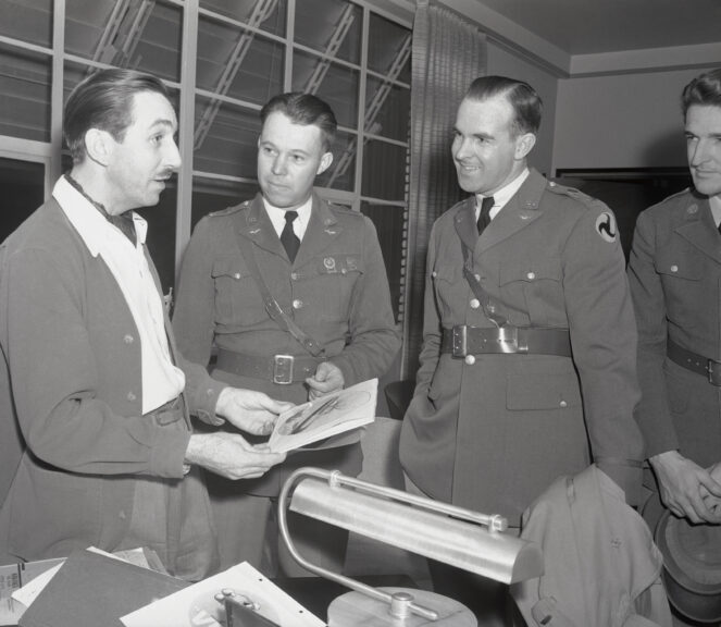 (Original Caption) Prompted by increasing requests from Army, Navy, and Air Corps branches, Walt Disney artists are now working on defense orders for service insignias. Walt Disney shows Air Corps officer Lieutenant Claude Pevey and insignia recently designed for the Navy's torpedo boats, known as the mosquito fleet. Bettmann/Contributor. Getty Images.
