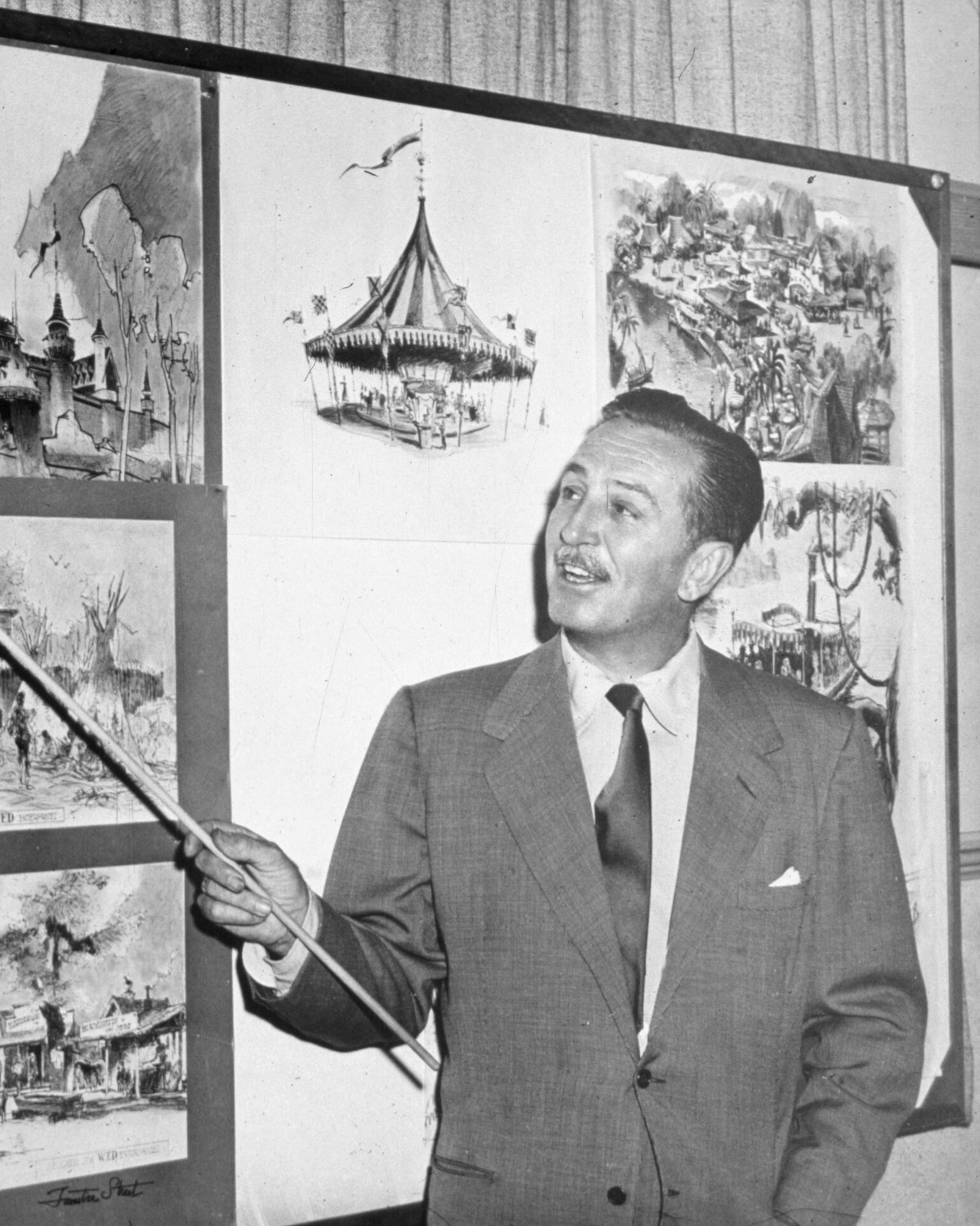 Disney Makes A Point American producer, director, and animator Walt Disney (1901 - 1966) uses a baton to point to sketches of Disneyland, 1955. (Photo by Hulton Archive/Getty Images)