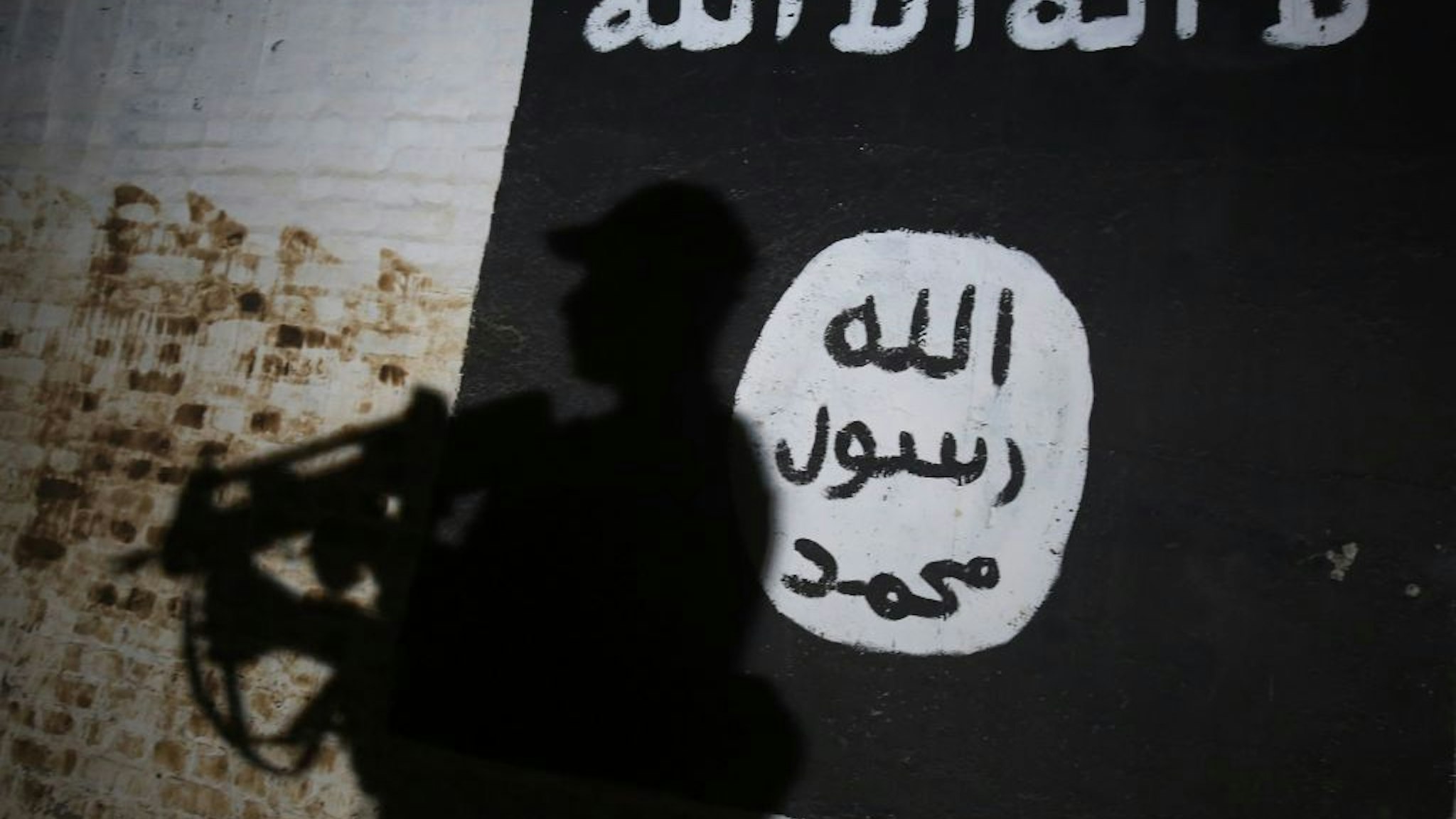 TOPSHOT - A member of the Iraqi forces walks past a mural bearing the logo of the Islamic State (IS) group in a tunnel that was reportedly used as a training centre by the jihadists, on March 1, 2017, in the village of Albu Sayf, on the southern outskirts of Mosul. Iraqi forces launched a major push on February 19 to recapture the west of Mosul from the Islamic State jihadist group, retaking the airport and then advancing north. / AFP PHOTO / AHMAD AL-RUBAYE (Photo credit should read