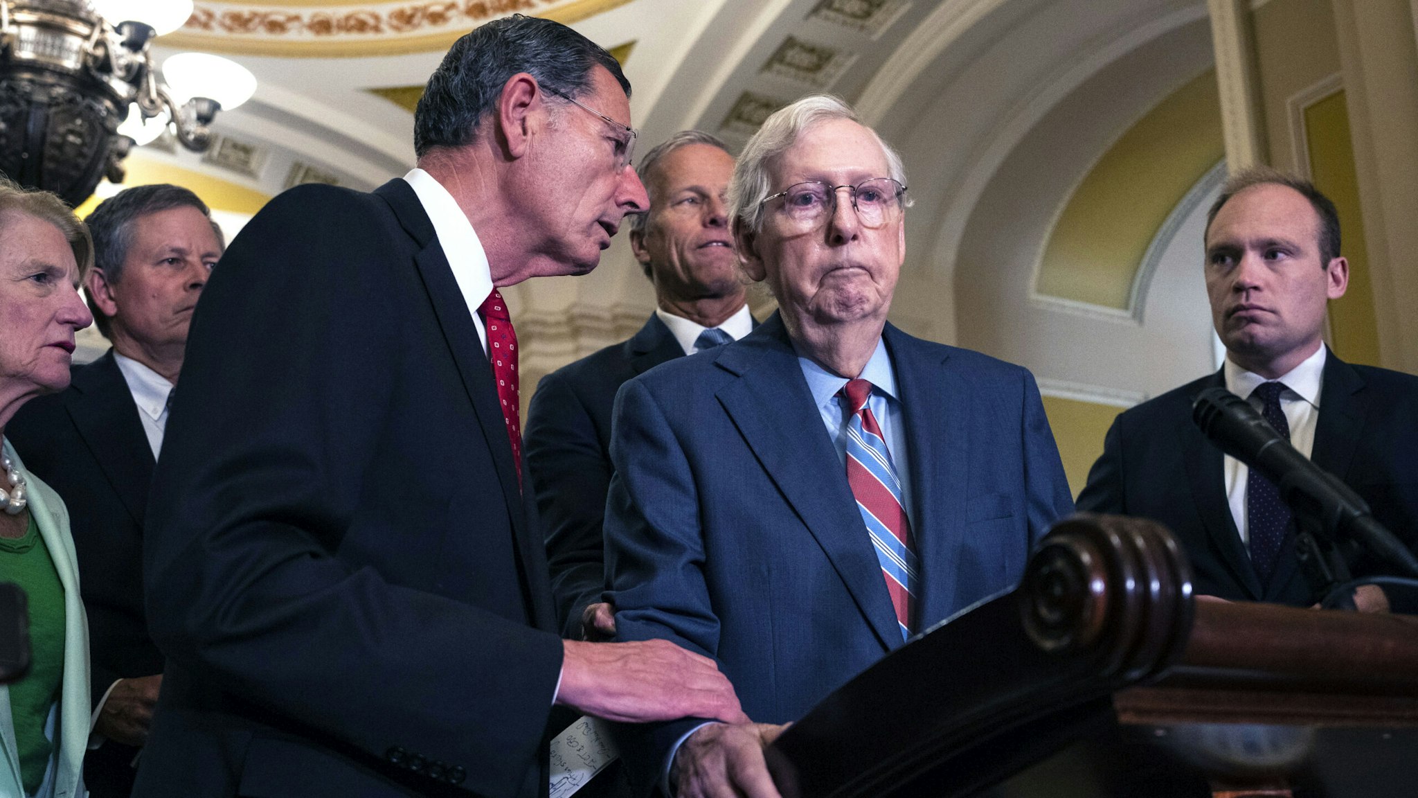 WASHINGTON, DC - JULY 26: (L-R) Sen. John Barrasso (R-WY) reaches out to help Senate Minority Leader Mitch McConnell (R-KY) after McConnell froze and stopped talking at the microphone during a news conference after a lunch meeting with Senate Republicans U.S. Capitol 26, 2023 in Washington, DC. Also pictured, L-R, Sen. Shelley Moore Capito (R-WV), Sen. Steve Daines (R-MT), Sen. John Thune (R-SD) and Sen. Joni Ernst (R-IA). McConnell was escorted back to his office and later returned to the news conference and answered questions.
