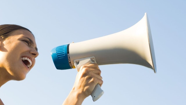 Woman shouting into megaphone, low angle view, cropped