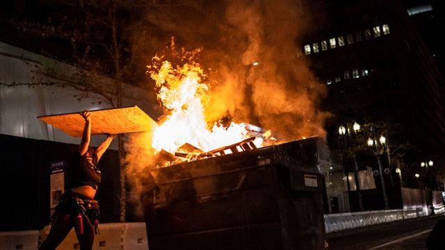 PORTLAND, OR - APRIL 16: A protester adds wood to a dumpster fire on April 16, 2021 in Portland, Oregon. Protests erupted Friday after Portland Police shot and killed a homeless man in Lents Park.