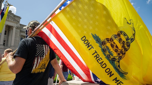 FRANKFORT, KY - AUGUST 28: A man with a Gadsden flag, a US flag, and a Confederate battle flag listens to a speaker during the Kentucky Freedom Rally at the capitol building on August 28, 2021 in Frankfort, Kentucky. Demonstrators gathered on the grounds of the capitol to speak out against a litany of issues, including Kentucky Gov. Andy Beshears management of the coronavirus pandemic, abortion laws, and the teaching of critical race theory. Demonstrators and speakers also refuted the legitimacy of the 2020 United State presidential election, claiming that former President Donald Trump won and should be reinstated. (Photo by Jon Cherry/Getty Images)