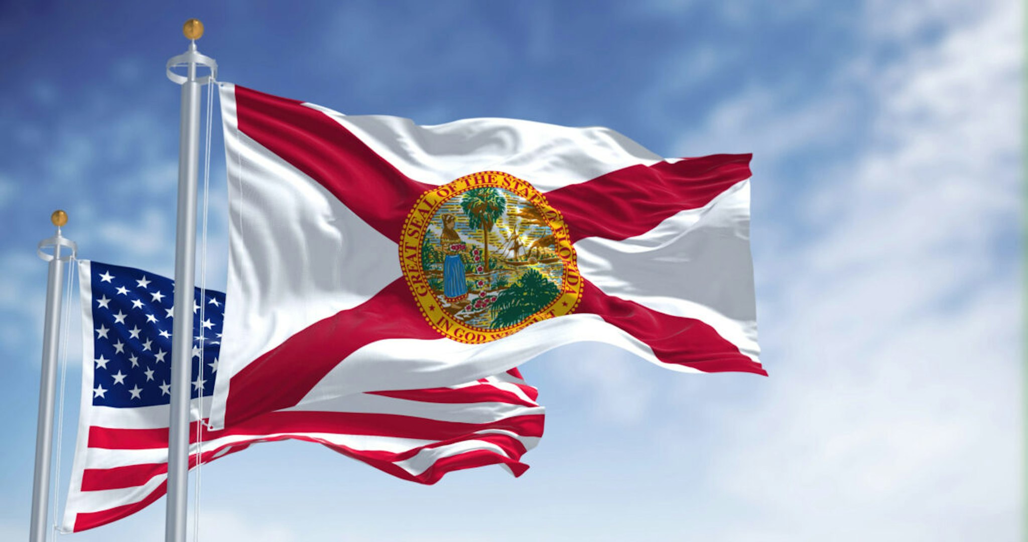 The Florida state flag waving along with the national flag of the United States of America. In the background there is a clear sky.