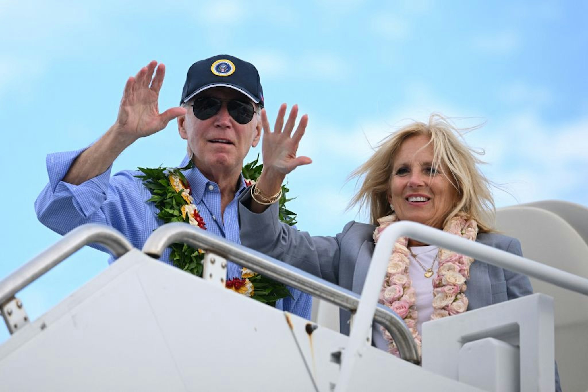 US President Joe Biden and US First Lady Jill Biden wear Hawaiian leis as they wave from Air Force One before departing Kahului Airport in Kahului, Hawaii, on August 21, 2023. The Bidens spent the day meeting with first responders, survivors, and local officials following deadly wildfires in Maui. (Photo by Mandel NGAN / AFP)