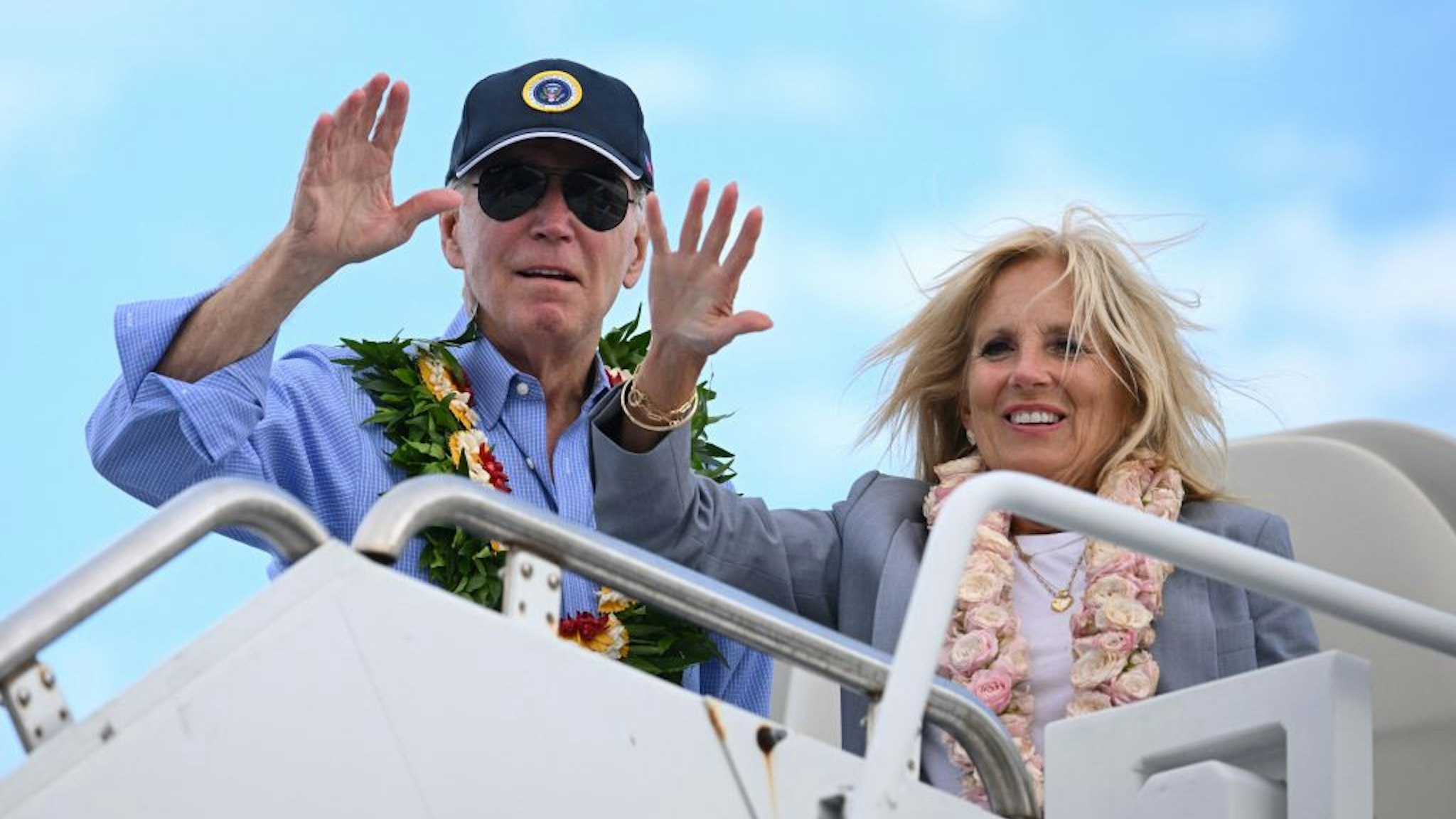 US President Joe Biden and US First Lady Jill Biden wear Hawaiian leis as they wave from Air Force One before departing Kahului Airport in Kahului, Hawaii, on August 21, 2023. The Bidens spent the day meeting with first responders, survivors, and local officials following deadly wildfires in Maui. (Photo by Mandel NGAN / AFP)